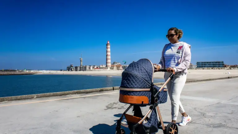 Frau mit Kinderwagen an der Küste neben einem Leuchtturm