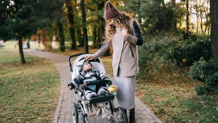 Mutter schiebt ihr Baby im Kinderwagen durch einen herbstlichen Park